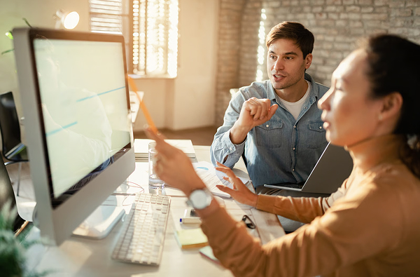 Team members discussing a digital product beside a desktop computer.